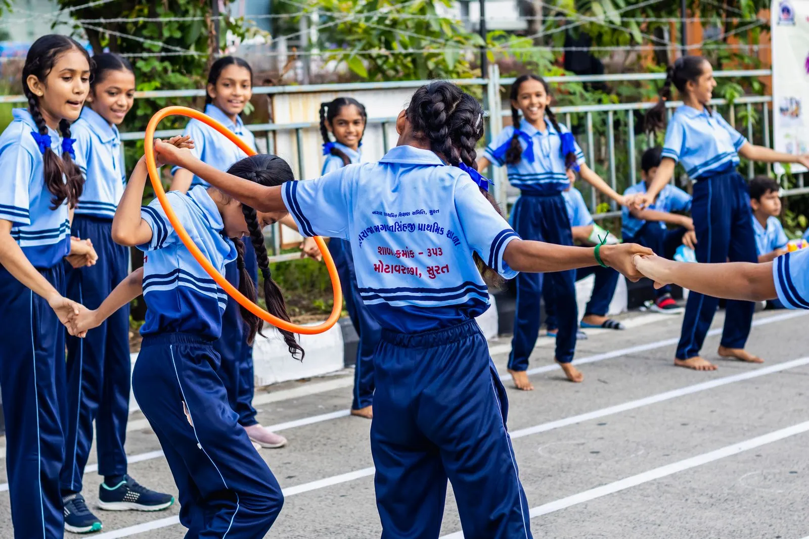 Group of schoolchildren enjoying outdoor games with hula hoops at a school event in Surat, India.